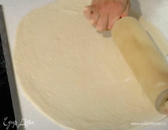 Тесто обмять, выложить на присыпанную мукой рабочую поверхность и раскатать в круг.
