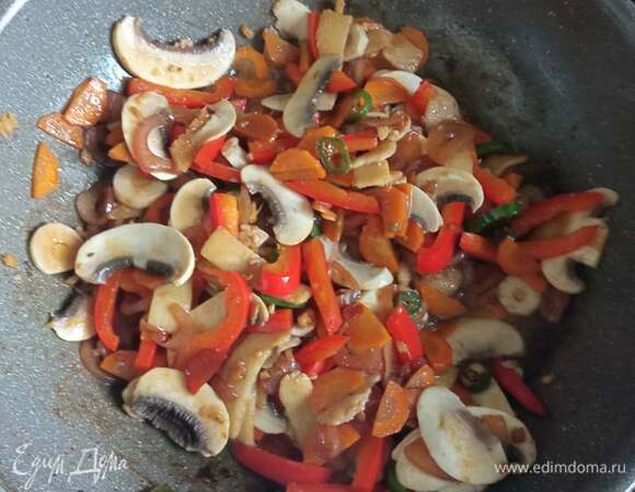 Добавить лук. Жарить 2 минуты. Добавить морковь. Жарить 2 минуты. Затем — перец, через 2 минуты — шампиньоны. Обжариваем еще 3 минуты. В процессе жарки постоянно помешиваем.