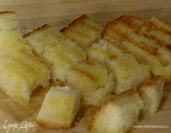 Приготовить крутоны: хлеб сбрызнуть с двух сторон оливковым маслом и обжарить на разогретой сковороде-гриль, затем нарезать на небольшие кусочки.