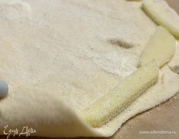 Перекладываем тесто на бумагу для выпекания. По краям пиццы выкладываем брусочки сыра, заворачиваем и плотно закрепляем.