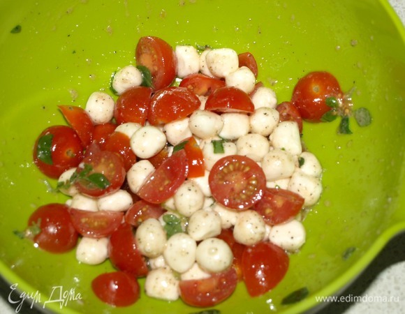 Помидоры черри разрезать на 2 или 4 части. Соединить в миске мини-моцареллу, томаты, мелко нарезанный зеленый базилик, соль, перец и оливковое масло. Перемешать.