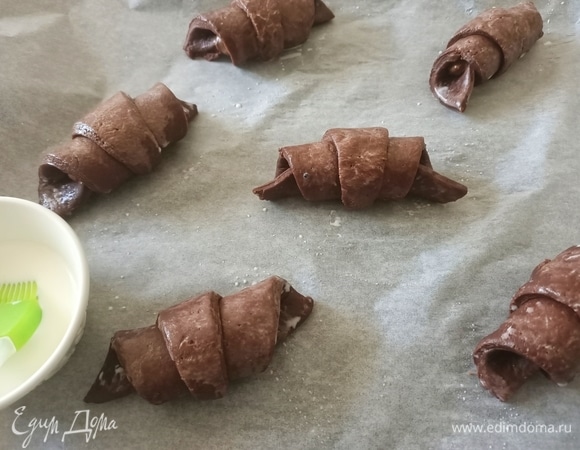 Противень застелить пергаментом. Выложить готовые круассаны. Сверху смазать молоком, накрыть пищевой пленкой и поставить в теплое место на 1 час.