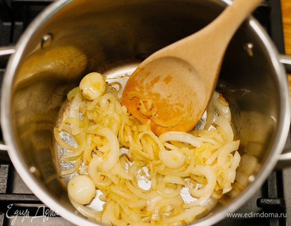В кастрюлю влить немного оливкового масла, пассеровать лук и очищенные целые зубчики чеснока.