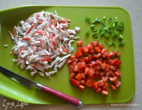 Помидоры (я использовала маленькие помидоры сорта «Сливка») нарежьте небольшими кубиками. Крабовые палочки разделите на волокна. Зеленый лук мелко нарежьте.