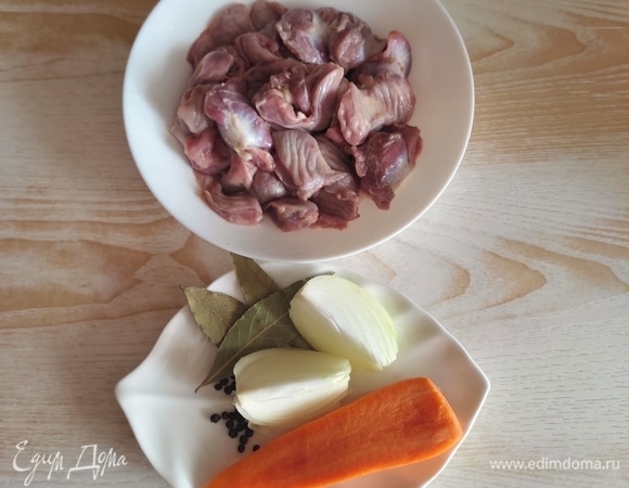 Подготовить куриные желудочки, а также половинку моркови и половинку луковицы, лавровый лист, перец горошком. Желудки залить водой и довести до кипения, затем бульон слить, снова залить чистой водой.