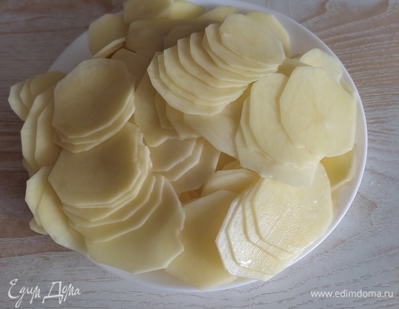 Картофель вымыть, очистить, нарезать тонкими слайсами. Удобнее это делать овощерезкой: чем тоньше слайсы, тем эффектнее будет выглядеть блюдо.