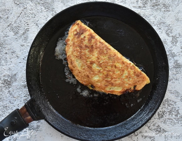 Деревянной лопаткой аккуратно приподнимаю свободный край кабачкового блинчика и сворачиваю его пополам, накрыв начинку. Обжарив с одной стороны получившийся чебурек, переворачиваю и до подрумянивания обжариваю с другой стороны.