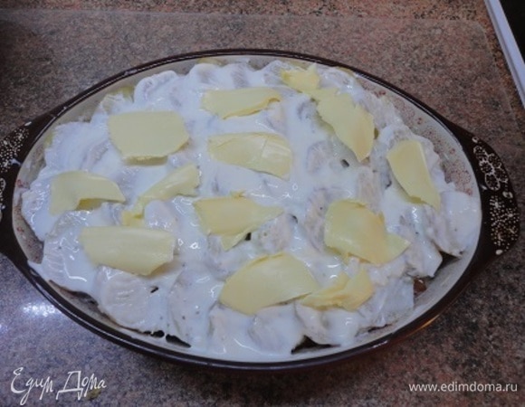 На рыбу выложить смесь лука со шпиком, затем — оставшуюся рыбу. Накрыть все второй половиной картофеля. Полить сливками и по поверхности распределить хлопья сливочного масла.
