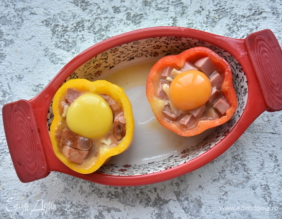 Подготовленные перцы устанавливаю в форму для запекания. Распределяю подготовленную начинку. Сверху столовой ложкой выкладываю аккуратно по целому желтку. Рядом с перцами укладываю «шляпки». Запекаю в духовке при 180°C 10 минут. При подаче сверху кладу кусочек сливочного масла и посыпаю рубленой зеленью.