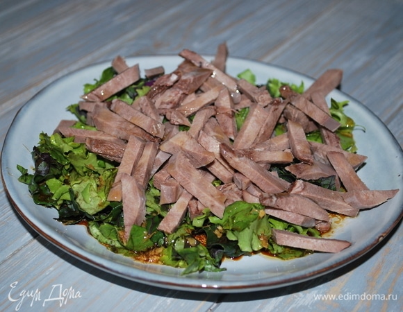 Полейте заправкой салатные листья, добавьте нарезанный язык, посыпьте свежемолотым черным перцем, перемешайте.