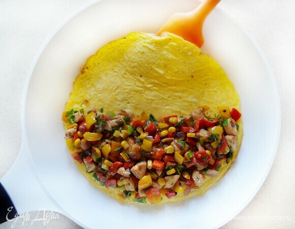 С помощью лопатки аккуратно отделите края омлета от сковороды. На одну половину омлета щедро выложите курицу с овощами, накройте пустой половинкой.