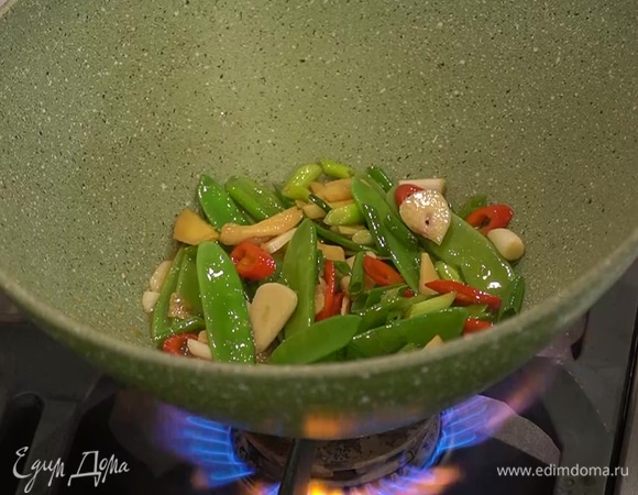 Масло из вока слить, влить оставшееся оливковое масло, всыпать нарезанные имбирь, перец и чеснок, влить соус, добавить зеленый горошек, зеленый лук и слегка обжарить все на сильном огне.