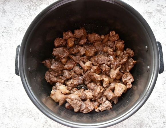 В чашу мультиварки помещаю курдучный жир. Выбираю в «Меню» режим «Жарка», готовлю 30 минут, помешивая, до вытапливания жира. Вливаю немного растительного масла. Добавляю говядину и продолжаю жарить до золотистости мяса.