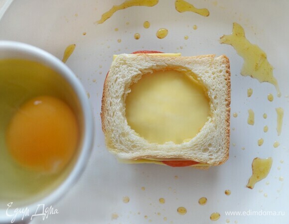 Потом — снова сыр, а сверху — кусок хлеба с отверстием. Кладем на сковороду, аккуратно вливаем небольшое яйцо (лучше предварительно его разбить в небольшую емкость) и готовим под закрытой крышкой на небольшом огне около 5 минут до готовности.