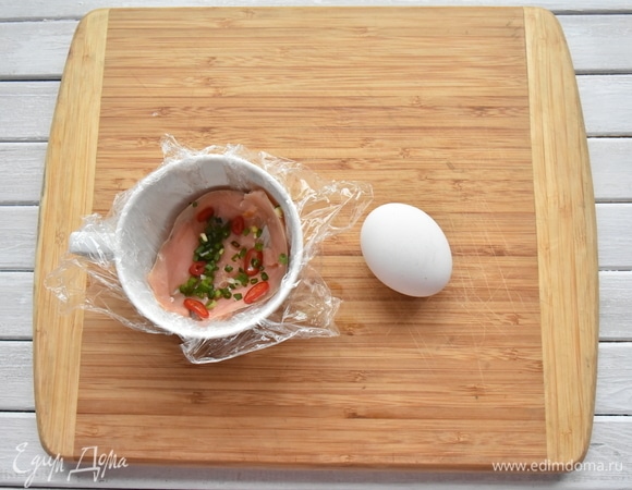 Выложила подготовленной пищевой пленкой дно и бока кружки, уложила ломтики рыбы, колечки красного острого перца и зеленого лука.
