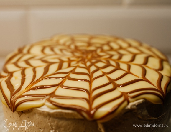 В кондитерском мешке с растопленным молочным шоколадом проделать небольшое отверстие и нарисовать спираль по белому верху торта, работая от центра к краю. Зубочисткой сразу же провести линии от центра к краям торта, а между ними — линии от краев торта к его середине.