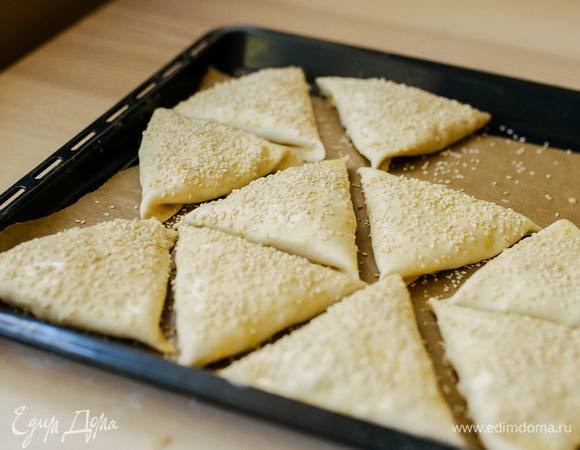 Слойки выложить швом вниз на противень, застеленный пергаментом. Смазать слегка взбитым яйцом и посыпать кунжутом.