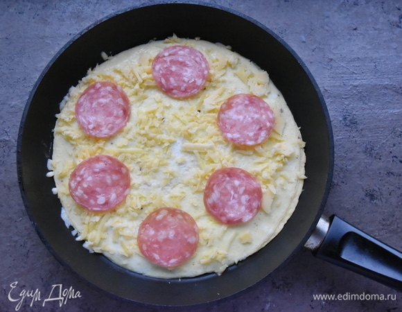 Пока поджаривается нижняя тортилья, на верхнем слое омлета распределяю оставшийся натертый сыр и ломтики салями.