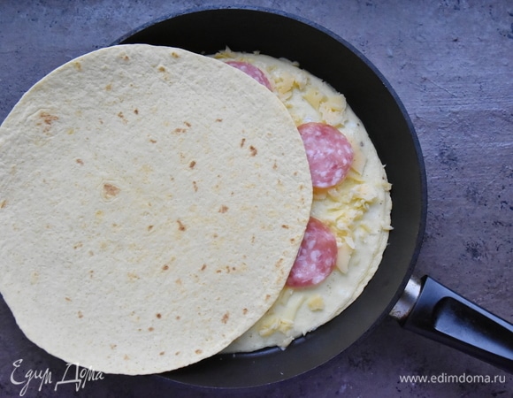 Сверху кладу вторую тортилью. Накрываю сковороду крышкой на пару минут — до расплавления сырного слоя.