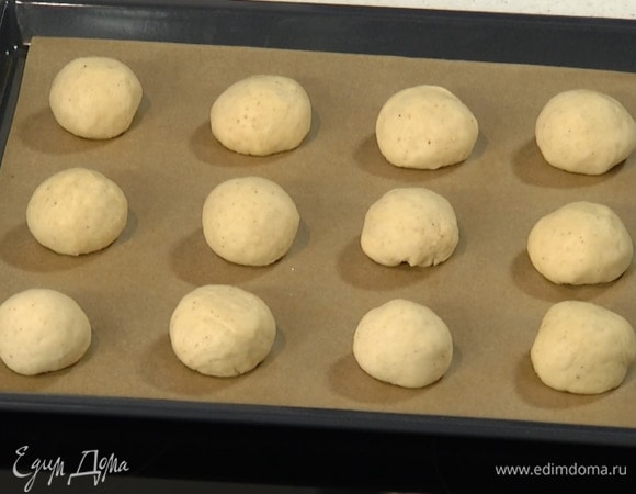 Подошедшее тесто выложить на присыпанную оставшейся мукой рабочую поверхность, скатать колбаску, разрезать на 12 частей и сформировать небольшие булочки, выложить их на застеленный бумагой для выпечки противень и оставить на 20 минут.