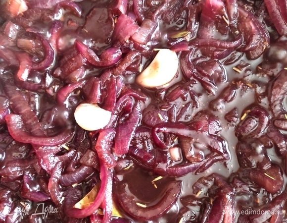 Добавляем к луку сначала мед, сахар и специи, хорошо размешиваем, далее вливаем винный уксус и вино. Зубчик чеснока разрезаем пополам. Снова размешиваем и дожидаемся, когда жидкость закипит. После чего убавляем огонь до минимума, накрываем сотейник крышкой и томим мармелад до полного испарения жидкости. Не забывайте периодически помешивать смесь.