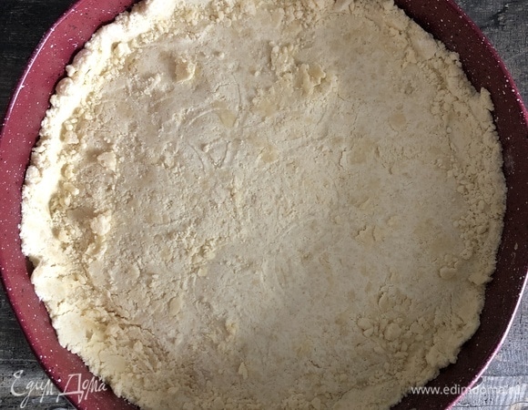 Крошку разделить на 2 части: побольше и поменьше. Большую часть выложить в форму, дно которой застелено пергаментом, и уплотнить руками или дном стакана.