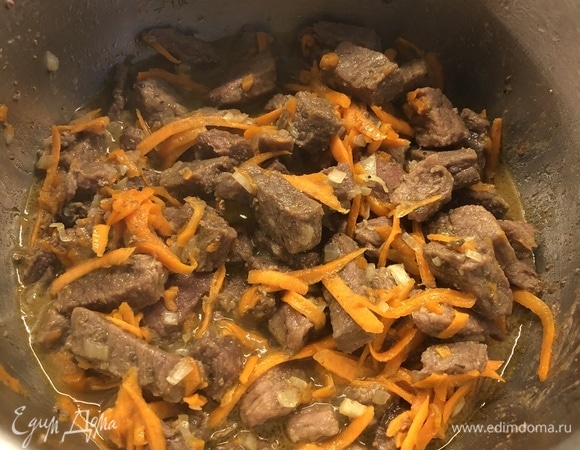 В разогретую кастрюлю с толстым дном наливаем небольшое количество растительного масла, нагреваем и выкладываем филе говядины, нарезанное средним кубиком. Обжариваем со всех сторон, добавляем лавровый лист и перец горошком, немного воды и тушим на среднем огне в течение 1,5 часов, пока мясо не станет мягким. При необходимости во время тушения добавляем еще воду. Через 1,5 часа к мясу добавляем нарезанный кубиком лук и натертую на крупной терке морковь.