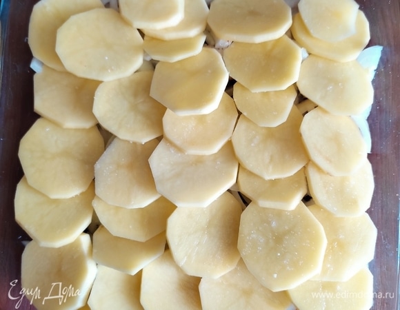 Очищенный картофель нарезать тонкими кружками и выложить на лук немного внахлест, чтобы картофель полностью закрыл луковый слой. Посолить, поперчить по вкусу.