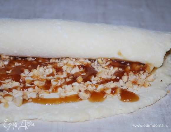 Разделите тесто на три части. Раскатайте тесто в тонкий пласт на посыпанной мукой поверхности. Посыпьте измельченными орехами и полейте ореховым соусом. Соус можно заменить коричневым сахаром.