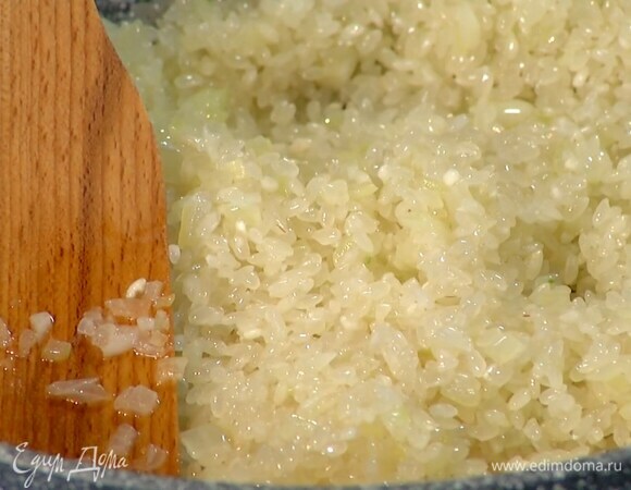 Чеснок почистить, мелко порубить, добавить в сковороду с луком и все еще немного обжарить, затем всыпать рис и, помешивая, обжарить его до прозрачности.