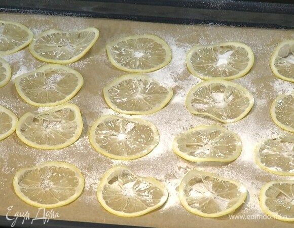 Два лимона для украшения нарезать очень тонкими кружками и выложить на противень, выстеленный бумагой для выпечки, через сито посыпать сахарной пудрой и запекать в разогретой духовке около часа.