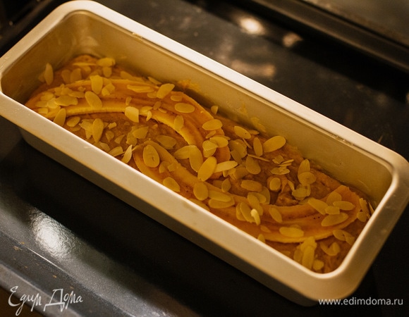 Форму смазать сливочным маслом, выложить тесто, банан разрезать вдоль и положить сверху. Посыпать миндальными лепестками.