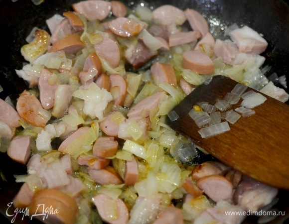 Добавьте в сковороду, перемешайте и обжаривайте все вместе до зарумянивания копченостей.