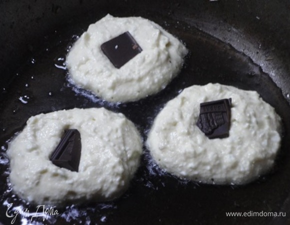 К жидким ингредиентам просеять муку с содой. Перемешать. Разогреть растительное масло на сковороде. Выложить ложкой тесто, сверху — по кусочку любимого шоколада, затем снова выложить еще немного теста. Жарить под крышкой на среднем огне. Перевернуть и продолжить готовить, только уже без крышки.