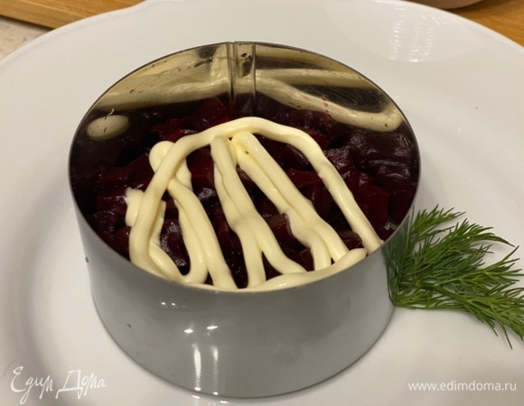 Собирать салат можно в кулинарном кольце. Для этого установите его на плоскую тарелку и начинайте собирать салат, но наоборот, следуя от последнего слоя классической селедки под шубой к первому. Сначала — свекла и немного майонеза.