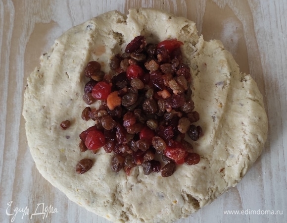 Руками разминаем комок теста в небольшой круг, выкладываем на середину сухофрукты и начинаем понемногу вмешивать их в тесто. В процессе можно припылять стол мукой. Но не увлекайтесь — не забейте тесто мукой! Максимум можно добавить 1–2 ст. л.