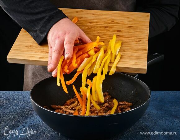 В сковороде разогрейте растительное масло и обжарьте говядину с луком. Добавьте перец и томите на огне 3 минуты.