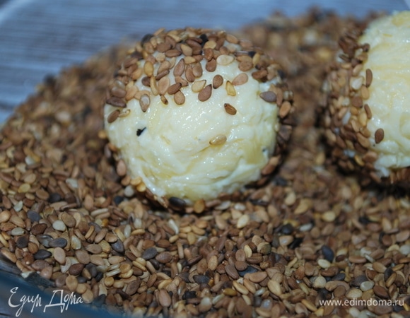 В миску насыпьте обжаренные семена кунжута. Руками сформируйте шарики из сыра и обваляйте со всех сторон в семенах кунжута. Из этого количества сыра получается примерно 12–15 шариков.