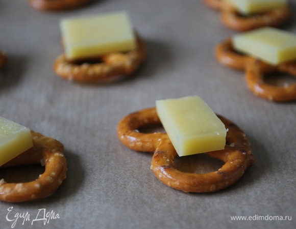 Примерно 30–40 г сыра нарежьте на небольшие пластинки, на брецель сверху положите кусочек сыра. Поставьте в духовку при 170°C на 3–4 минуты, чтобы сыр подтаял.