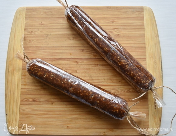 Из получившейся массы формирую колбаски, обваливаю часть в оставшемся кунжуте, а часть оставляю без посыпки. Оборачиваю пленкой и закрепляю концы. Кладу финиковый десерт в холодильник для стабилизации.