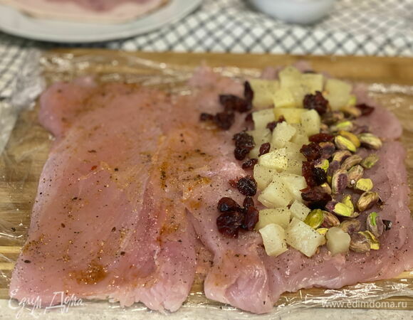 Переверните филе вместе с пленкой на другую сторону. Посолите, поперчите, добавьте немного сушеного чеснока, смажьте соусом чили и разложите начинку: ананас, клюкву и очищенные фисташки.