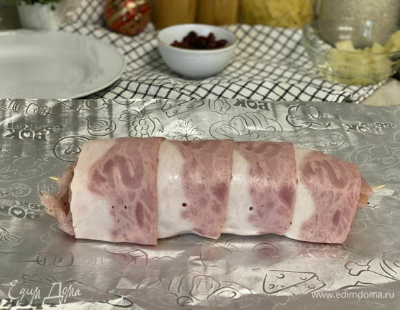 Плотно сверните рулет: двигайтесь от края с начинкой — к свободному. Пищевая пленка должна остаться снаружи, она больше не понадобится. Края скрепите зубочисткой.<br />
Оберните рулет беконом. 