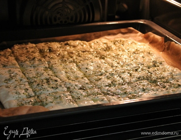 На противень кладем лист пергамента. Разравниваем на весь противень лепешку. Сверху смазываем чесноком с петрушкой. Ставим в духовку на 180°C. Выпекаем примерно 30 минут.