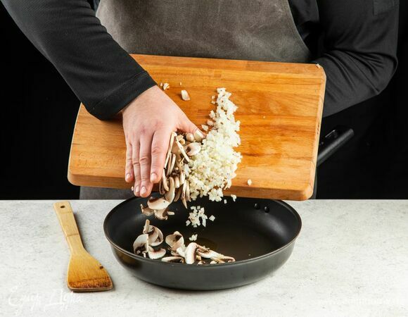 В сковороде разогрейте оливковое масло, выложите лук и грибы. Обжаривайте около 5 минут.