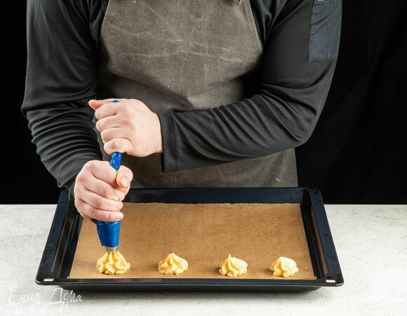 Наполните кондитерский мешок заварным тестом. С помощью наконечника выложите аккуратные холмики теста на противень, застеленный пергаментом. Оставьте между каждой заготовкой достаточно места.<br />
Выпекайте в разогретой до 180°C духовке около 35 минут.