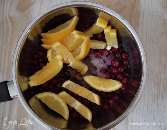 В ковш выложить клюкву, апельсин, нарезанный кусочками, добавить сахар и специи. Поставить на средний огонь.