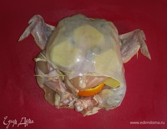 Затем внутрь куриной тушки положить апельсин и репчатый лук. Закрепить кожу тушки зубочистками, а ножки связать кулинарной нитью, чтобы начинка не выпадала.