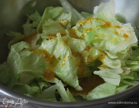 Порвите салат руками, выложите в чашу и полейте половиной заправки.