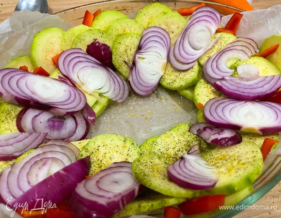 Нарежьте красный лук кольцами, а красный перец — недлинными ломтиками. Выложите все поверх кабачков.