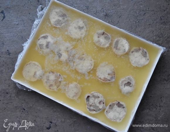 Для удобства извлечения заливного из формы рекомендую выстелить ее пищевой пленкой. Выложить нарезанные колбаски в форму на расстоянии друг от друга. Растворить быстрорастворимый желатин в 100 мл теплого бульона, после чего соединить его с оставшимся бульоном и перемешать. Залить бульон в форму. Поставить заливное в холодильник до застывания. Перед подачей нарезать заливное на порционные кусочки.